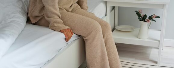 A woman sitting on a bed worrying that she has had a miscarriage.