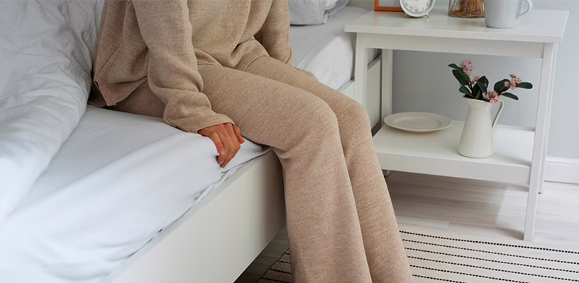 A woman sitting on a bed worrying that she has had a miscarriage.