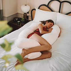 Pregnant woman sleeping in bed with the Yana 360 Degree Body Pillow wrapped around her.