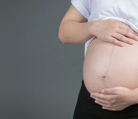 Pregnant woman placing her hands on her belly in anticipation of her water breaking.