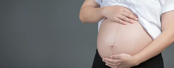 Pregnant woman placing her hands on her belly in anticipation of her water breaking.
