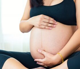 Pregnant women sitting cross-legged with her hands on her belly, thinking about the position of her placenta.