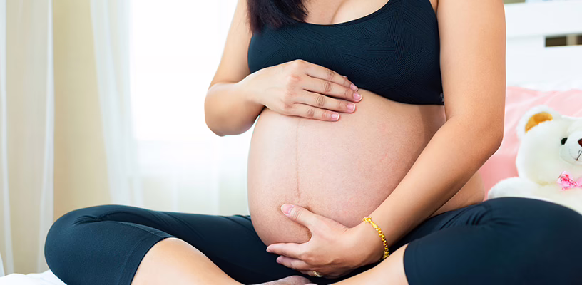 Pregnant women sitting cross-legged with her hands on her belly, thinking about the position of her placenta.