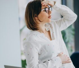 Woman holding her hand to her forehead, feeling forgetful due to pregnancy brain.