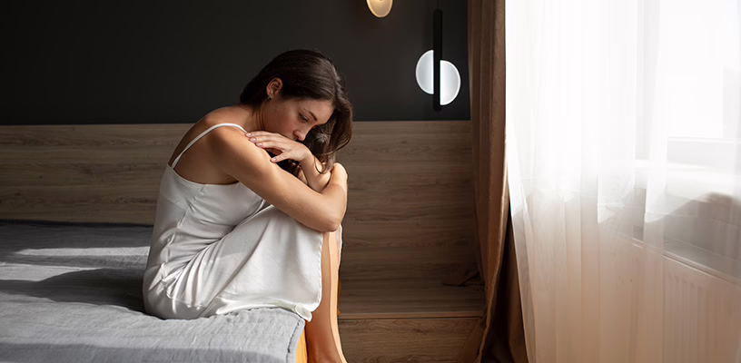 Woman sitting on the edge of her bed with a sad expression after experiencing early pregnancy loss.