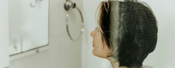 Woman looking at herself in the mirror, noticing the development of melasma.
