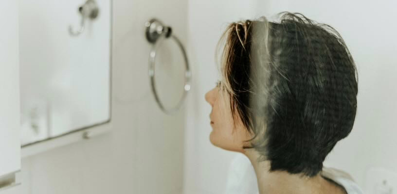 Woman looking at herself in the mirror, noticing the development of melasma.