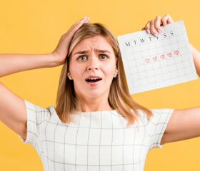 Woman looking confused and holding up a calendar, trying to determine if she's pregnant despite her irregular periods.