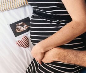 Pregnant mom being hugged around her baby bump by her partner.