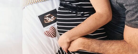 Pregnant mom being hugged around her baby bump by her partner.