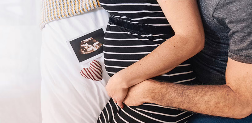 Pregnant mom being hugged around her baby bump by her partner.
