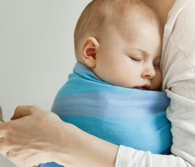Woman holding her baby while looking at a baby tracker app on her phone.