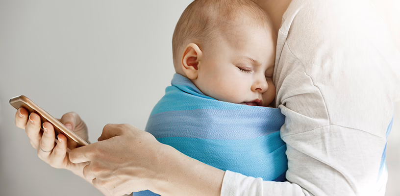 Woman holding her baby while looking at a baby tracker app on her phone.