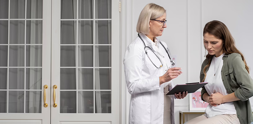Woman clutching her stomach while speaking to her doctor, as she's noticed the signs of an ectopic pregnancy.