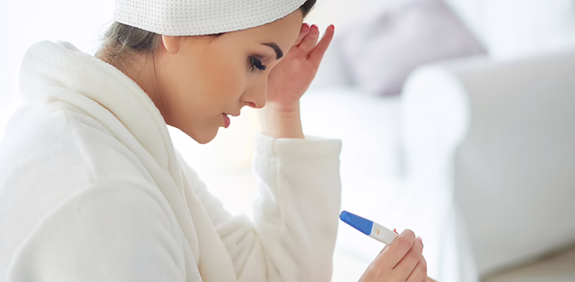 Anxious woman staring down at faint positive result on ovulation test.