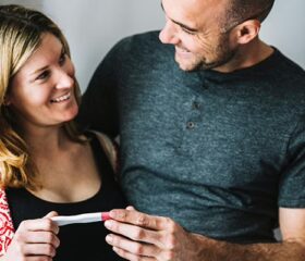A couple stand look at each other while holding an early-detection pregnancy test.