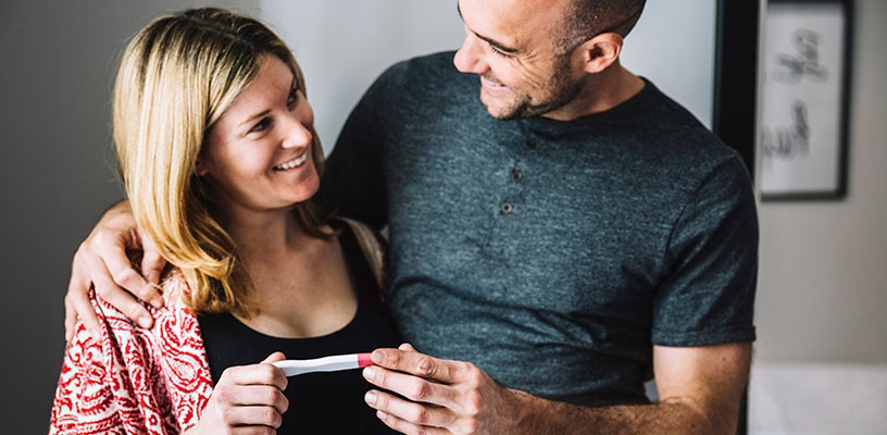 A couple stand look at each other while holding an early-detection pregnancy test.