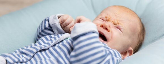 Upset baby purple crying while lying on blanket.