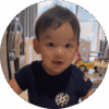 12-month-old baby standing up with toys and crib in the background.