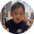 12-month-old baby standing up with toys and crib in the background.