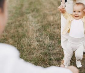 An 11-month-old baby being supported by her parents and taking a few steps.