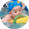 Six-month-old baby in pool wearing swimming cap and floating on pool noodle.