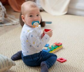 An 8-month-old baby sitting up and playing with a pacifier in.