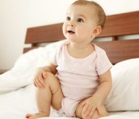 A 9-month-old baby sitting up on a bed.