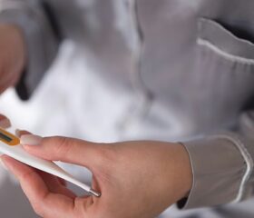Woman in bed looking at her basal body temperature on a thermometer.