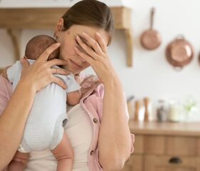 A new mother carrying her baby, while feeling overwhelmed as a result of postpartum depression.