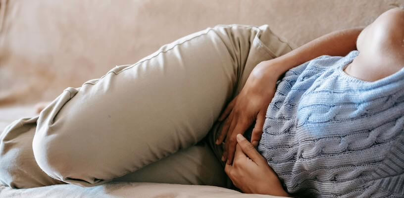 Pregnant woman with nausea holding her stomach while lying down on couch.