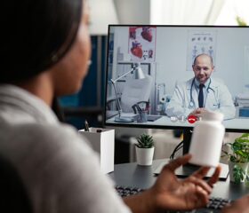 Woman sitting at her computer and talking to a doctor on a telehealth platform.