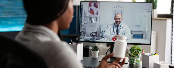 Woman sitting at her computer and talking to a doctor on a telehealth platform.