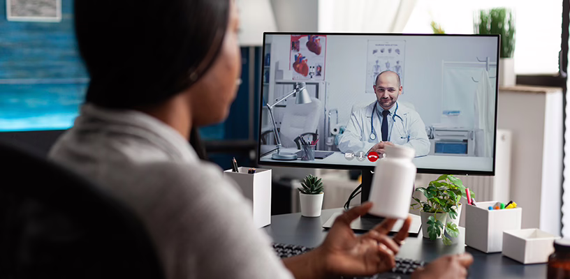 Woman sitting at her computer and talking to a doctor on a telehealth platform.