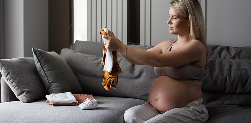 A pregnant women who's entered her third trimester organizing her baby's clothes.