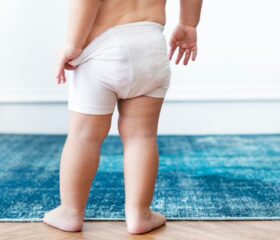 Toddler standing on rug and tugging down down his pull-up diaper.
