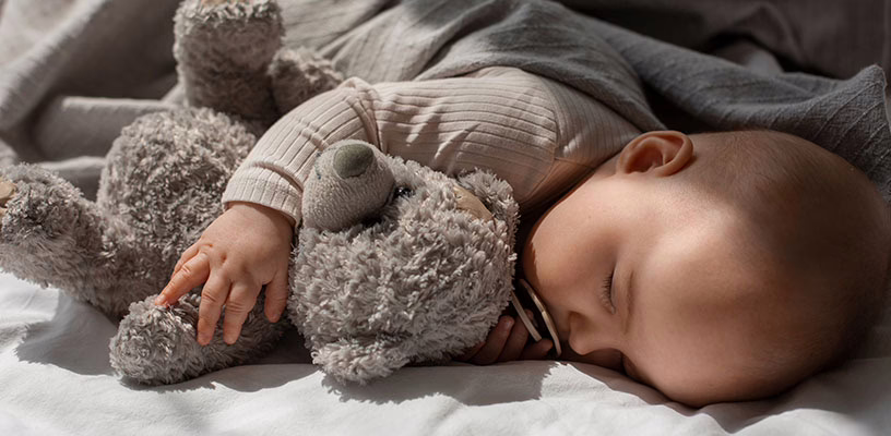 Baby sleeping quietly while hugging a teddy bear.