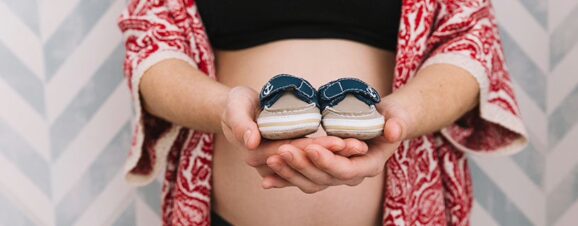 Pregnant woman holding two baby slippers.