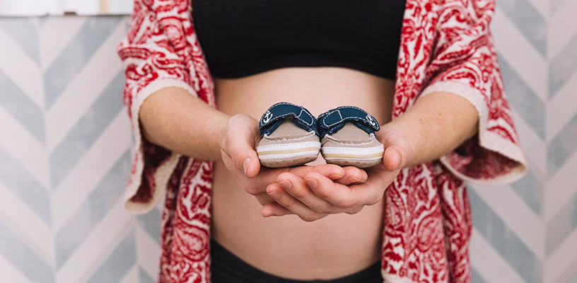 Pregnant woman holding two baby slippers.