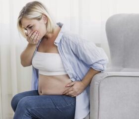 Pregnant woman holding her mouth as if about to vomit, due to her heightened sense of smell.