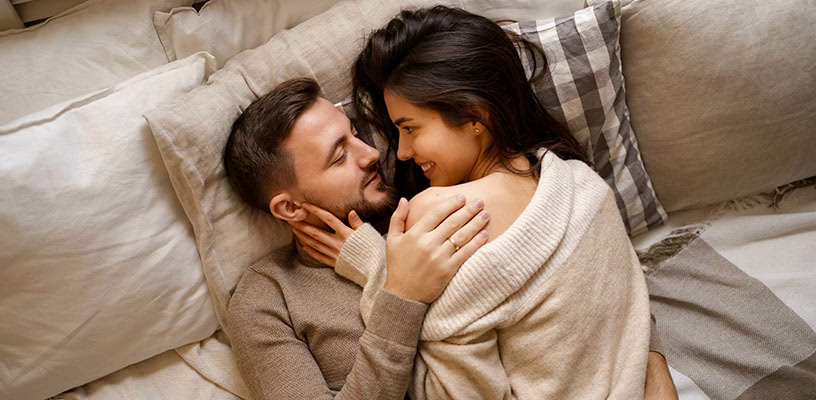 A man and a woman intimately lying on a bed as they want to try getting conceiving.