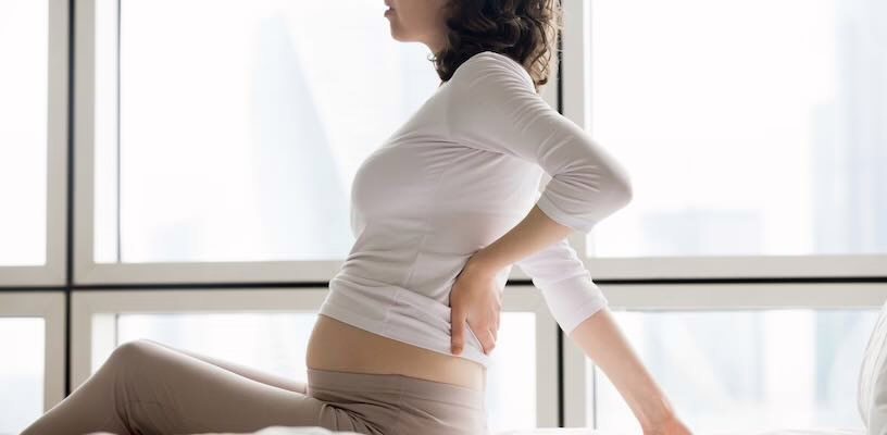 Pregnant woman sitting up and massaging her lower back for pain relief.