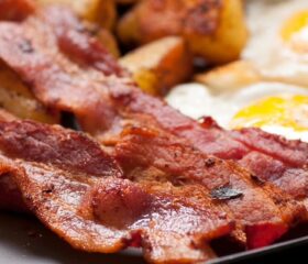 A breakfast plate of fried bacon, potato wedges, and sunny side up eggs.