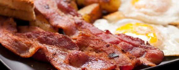 A breakfast plate of fried bacon, potato wedges, and sunny side up eggs.