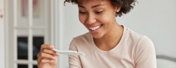 Woman with PCOS smiling down at a positive pregnancy test.