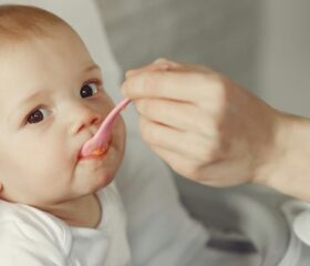 Mother feeding a baby meat for the first time with a spoon.