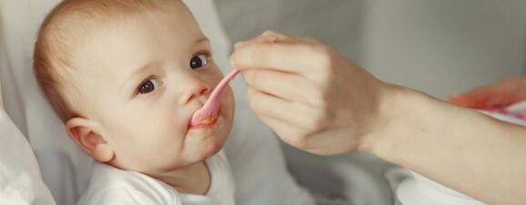 Mother feeding a baby meat for the first time with a spoon.