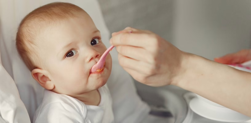 Mother feeding a baby meat for the first time with a spoon.