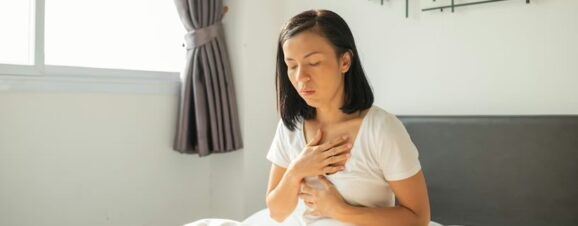 Pregnant woman sitting in bed and clutching her chest as a result of heartburn.