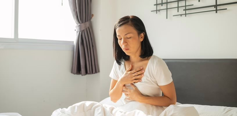 Pregnant woman sitting in bed and clutching her chest as a result of heartburn.